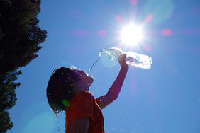 Image d'une femme qui boit de l'eau sous un soleil accablant